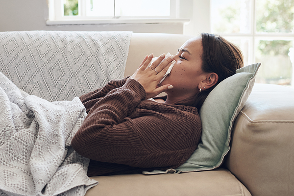 woman blowing her nose lying on couch sick with flu